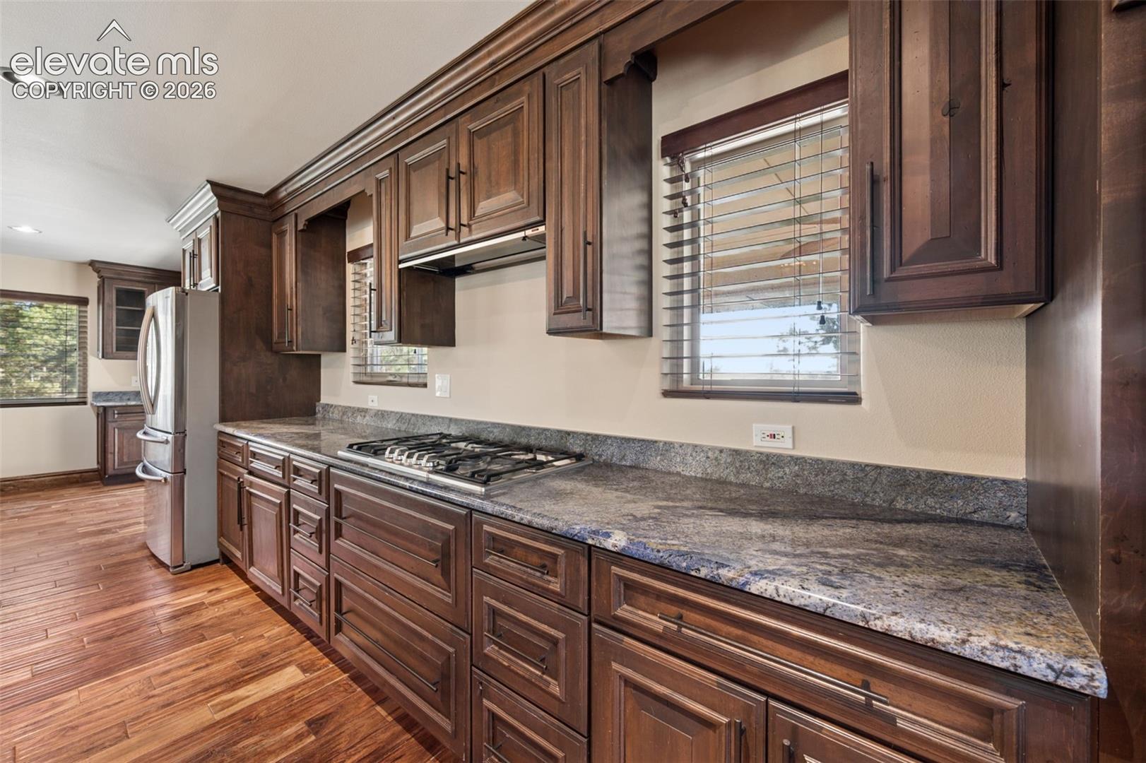Kitchen featuring dark wood cabinetry, stone-surface countertops, integrated gas cooktop, wood-finish flooring, and recessed lighting