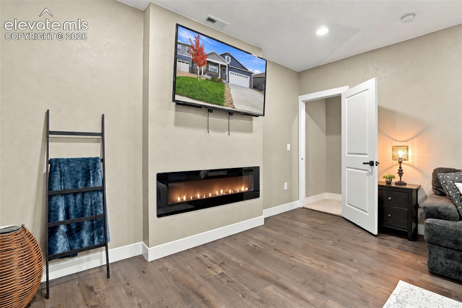 Linear electric fireplace with a black glass surround, wood-finish flooring, and recessed ceiling lighting