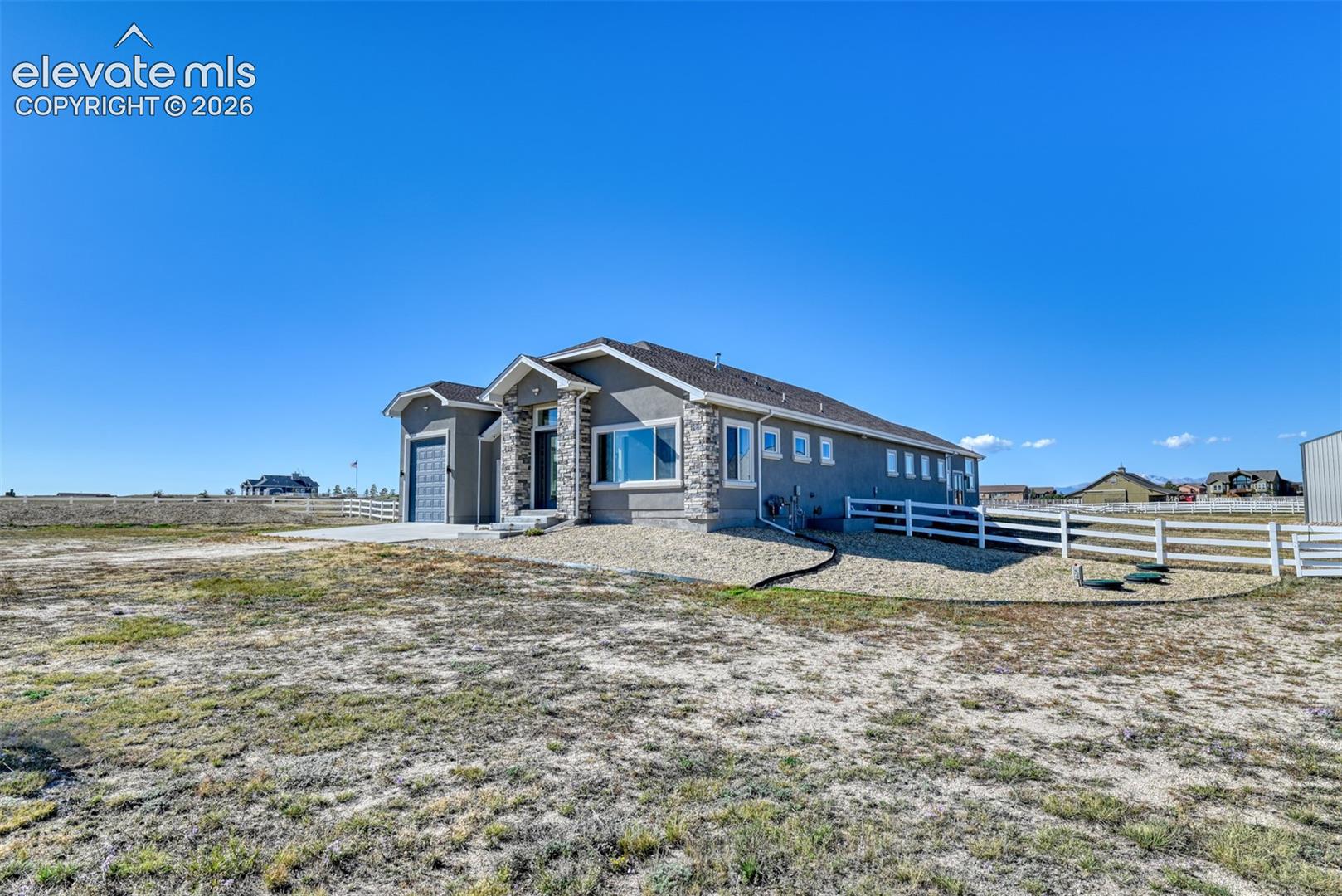 Ranch-style residence featuring a stucco and stone exterior, attached RV garage & two-car garage, white fencing, and a gravel perimeter.