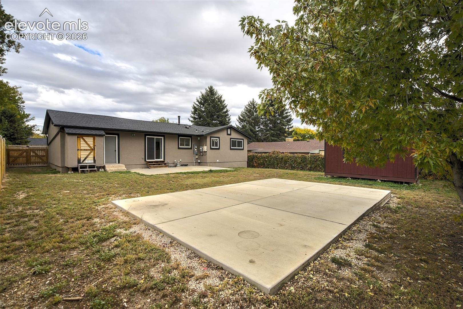 Rear exterior featuring a concrete patio, detached storage structure, and fenced perimeter