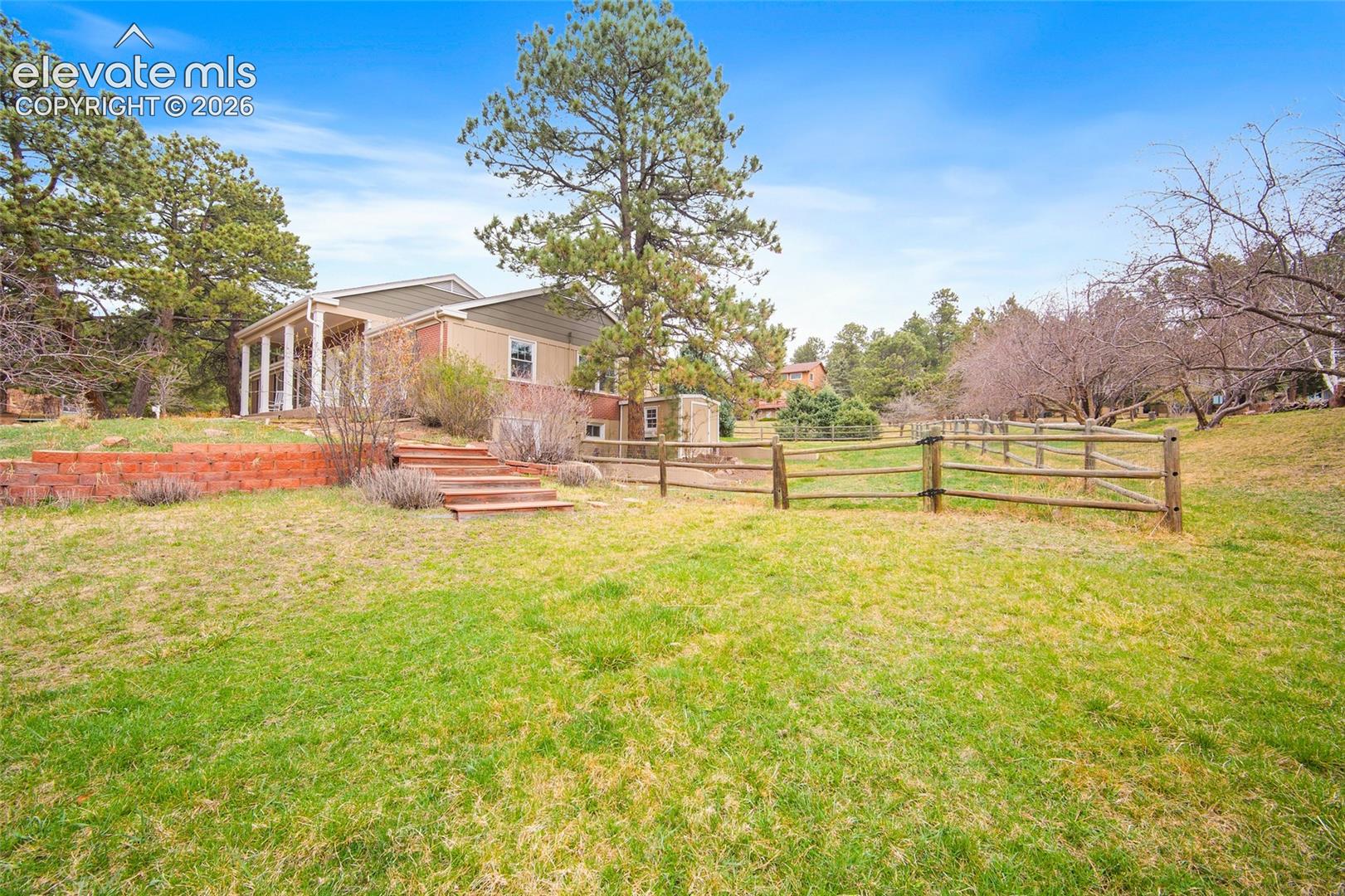 Expansive grounds featuring a tiered brick retaining wall, wooden staircase, split-rail fencing, and mature evergreen trees