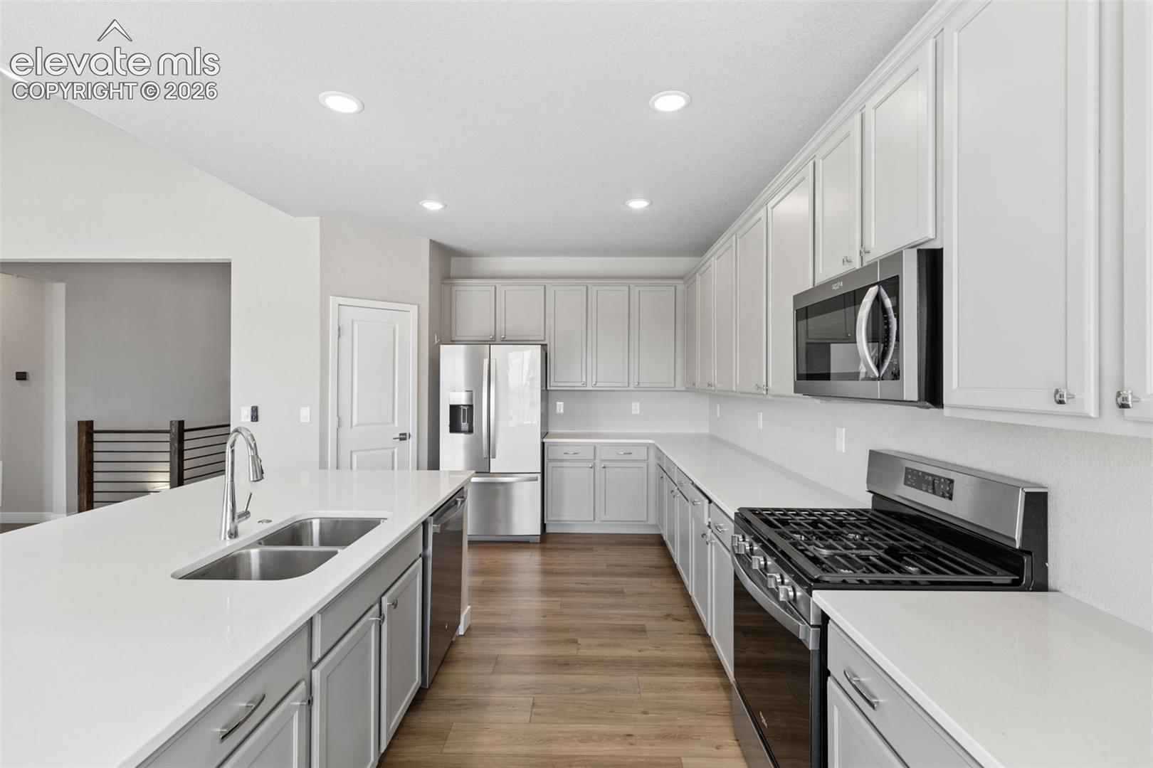 Kitchen featuring white shaker-style cabinetry, solid-surface countertops, wood-finish flooring, stainless steel appliances, and recessed lighting