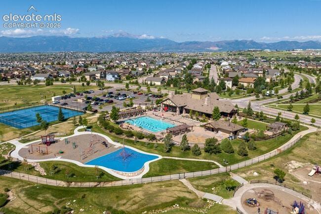 Community recreational complex featuring an outdoor swimming pool, paved tennis courts, play structures, and mountain backdrop