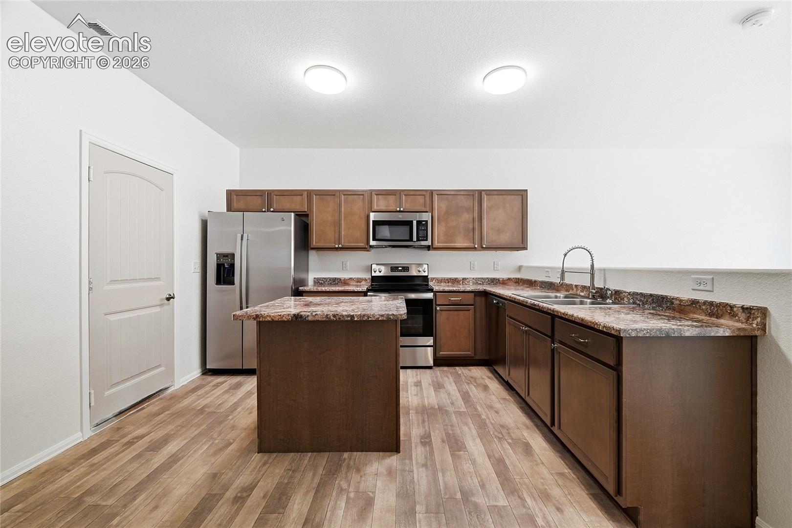Kitchen featuring wood-finish cabinetry, a central island, stone-patterned countertops, stainless steel appliances, and wood-finish flooring