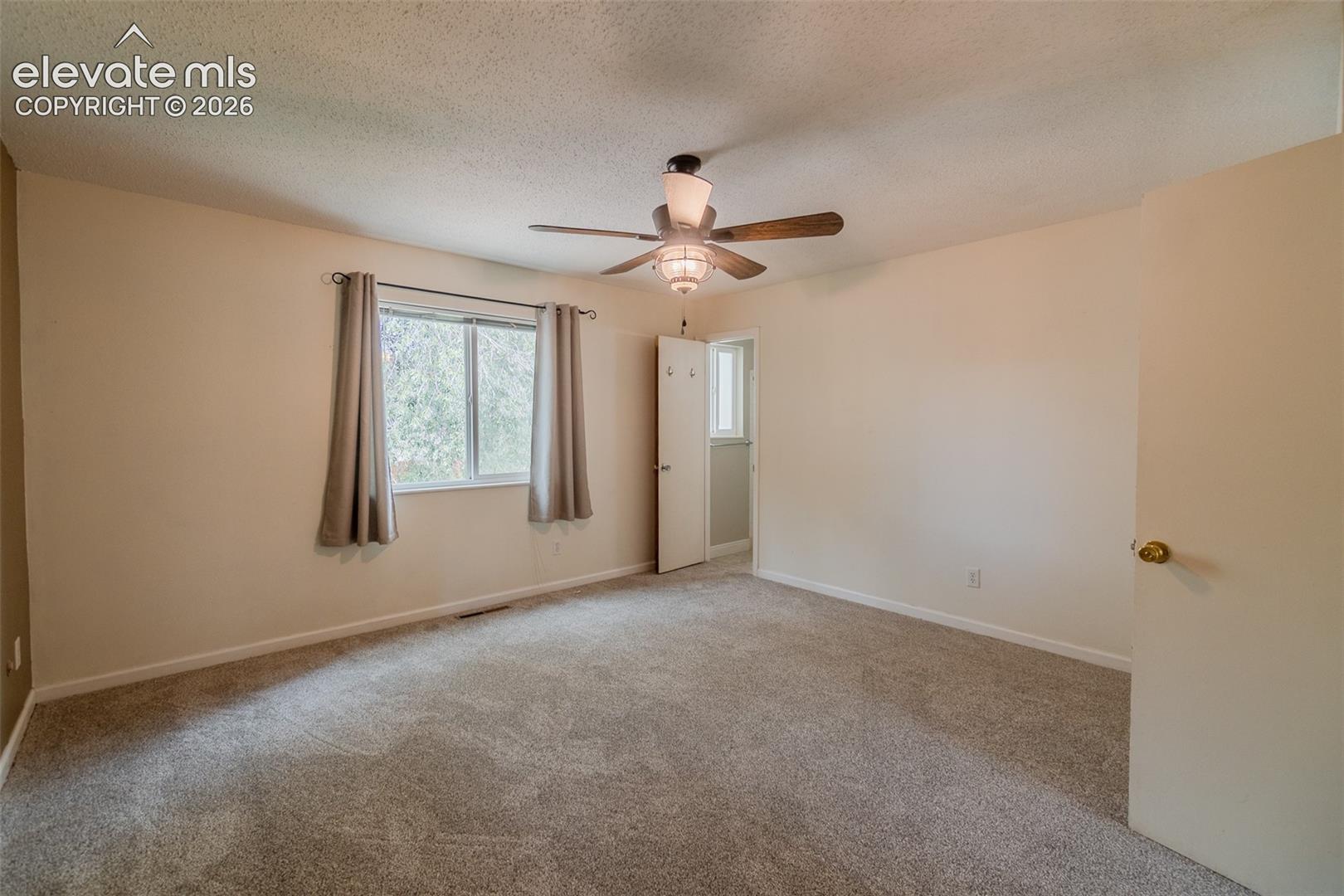 Spacious room featuring neutral carpeting, a ceiling fan with integrated lighting, and a double-hung window