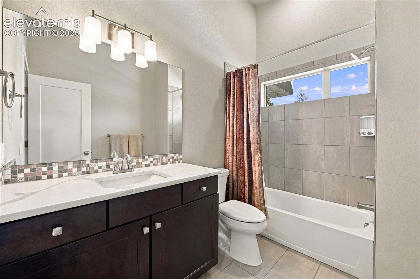 Bathroom featuring a dark wood-finish vanity with a light-toned countertop, undermount sink, multi-colored mosaic tile backsplash, and a tub-shower combination with large-format wall tile