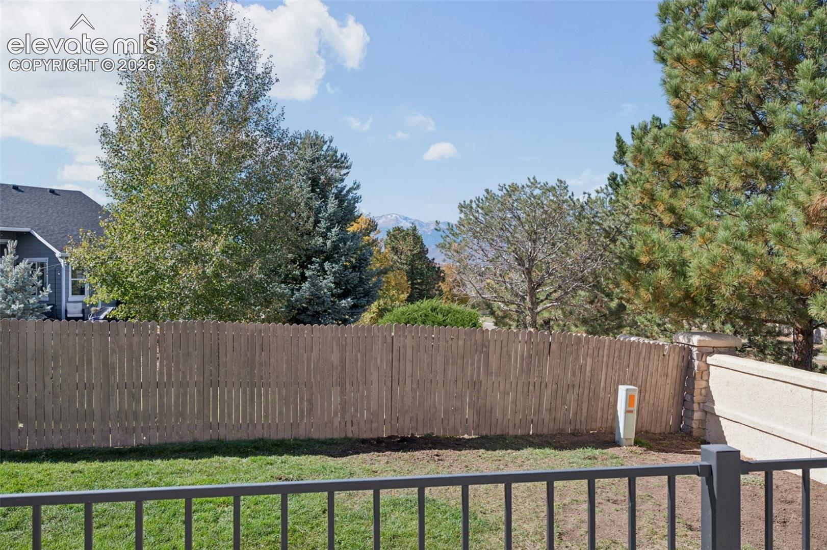 Backyard featuring a grass lawn, metal fencing, wood-slat privacy fencing, mature trees, and mountain scenery