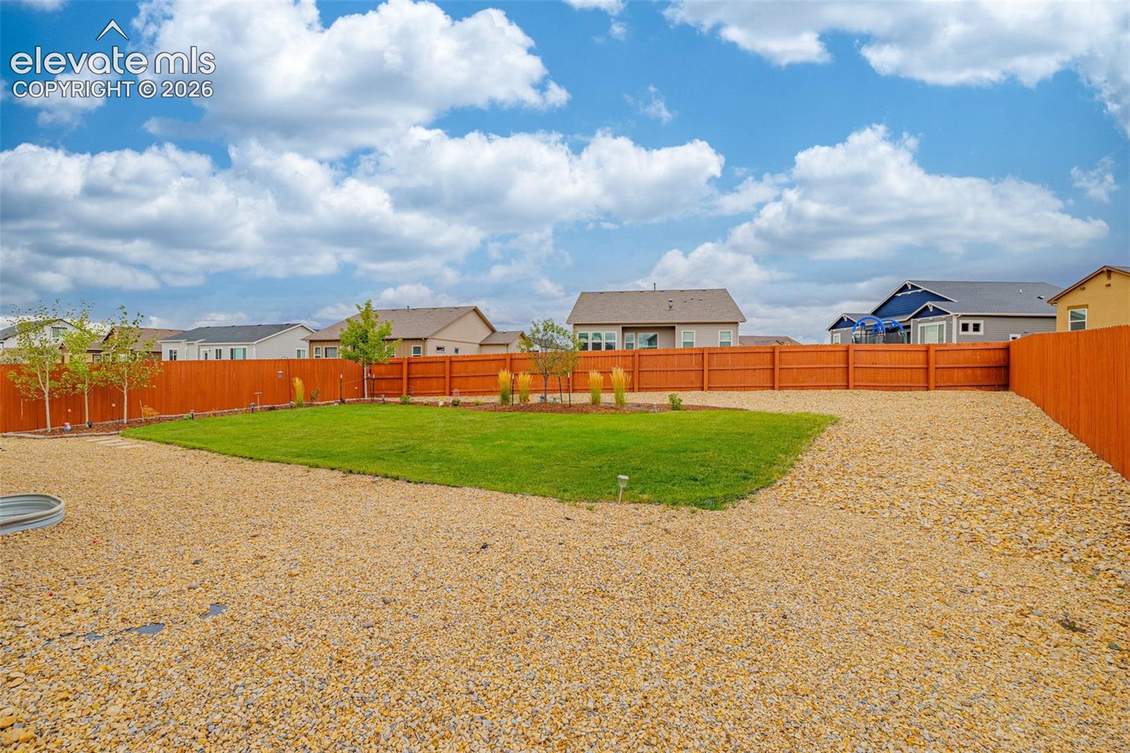 Expansive backyard featuring a manicured lawn, gravel landscaping, and wood privacy fencing