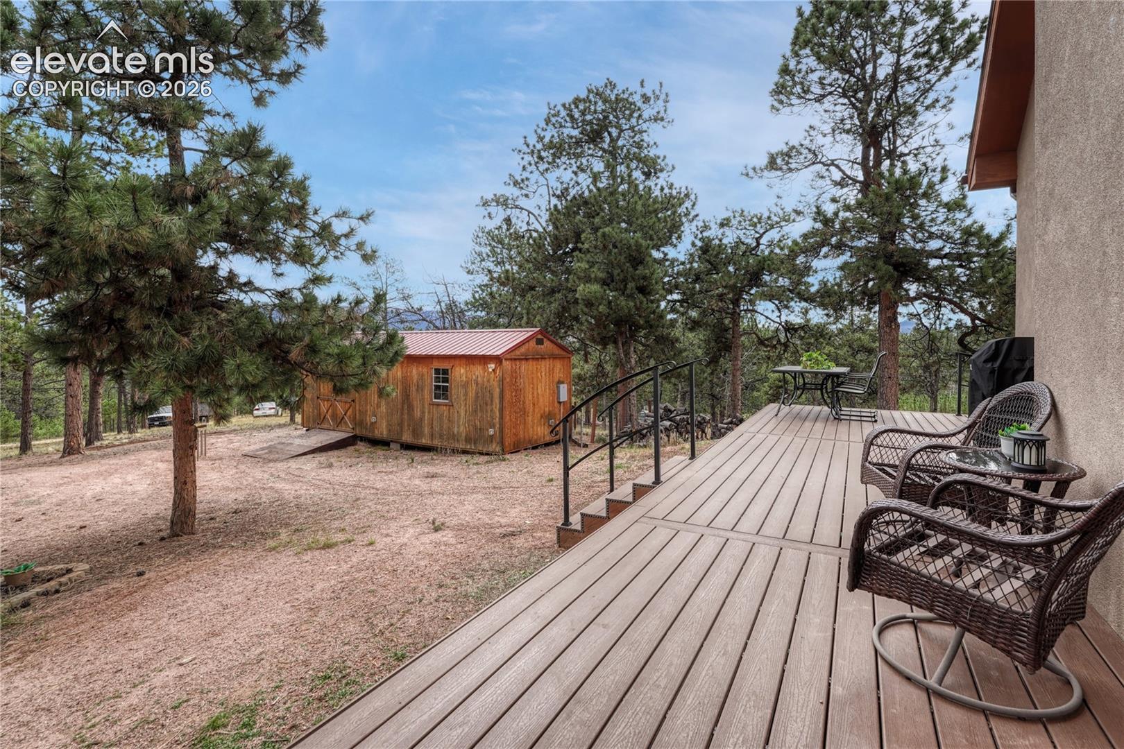 Elevated deck featuring composite decking, black metal railings, a wooden storage structure, and mature pine trees