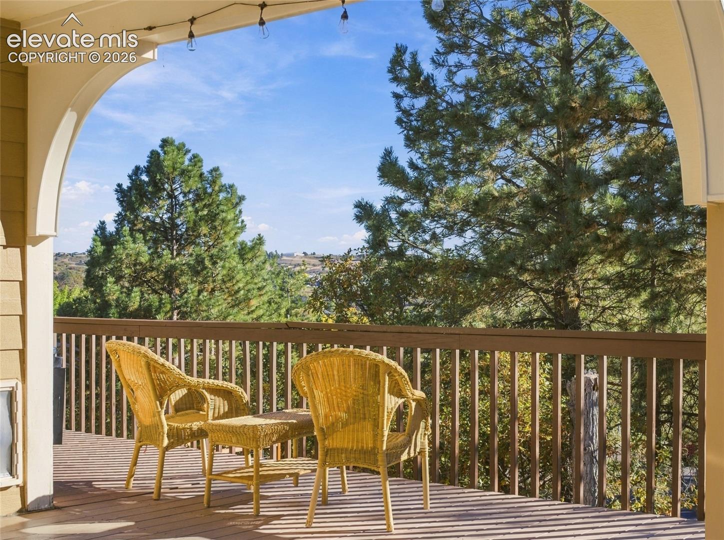 Covered deck featuring arched structural detailing, vertical picket railing, and surrounding woodland scenery