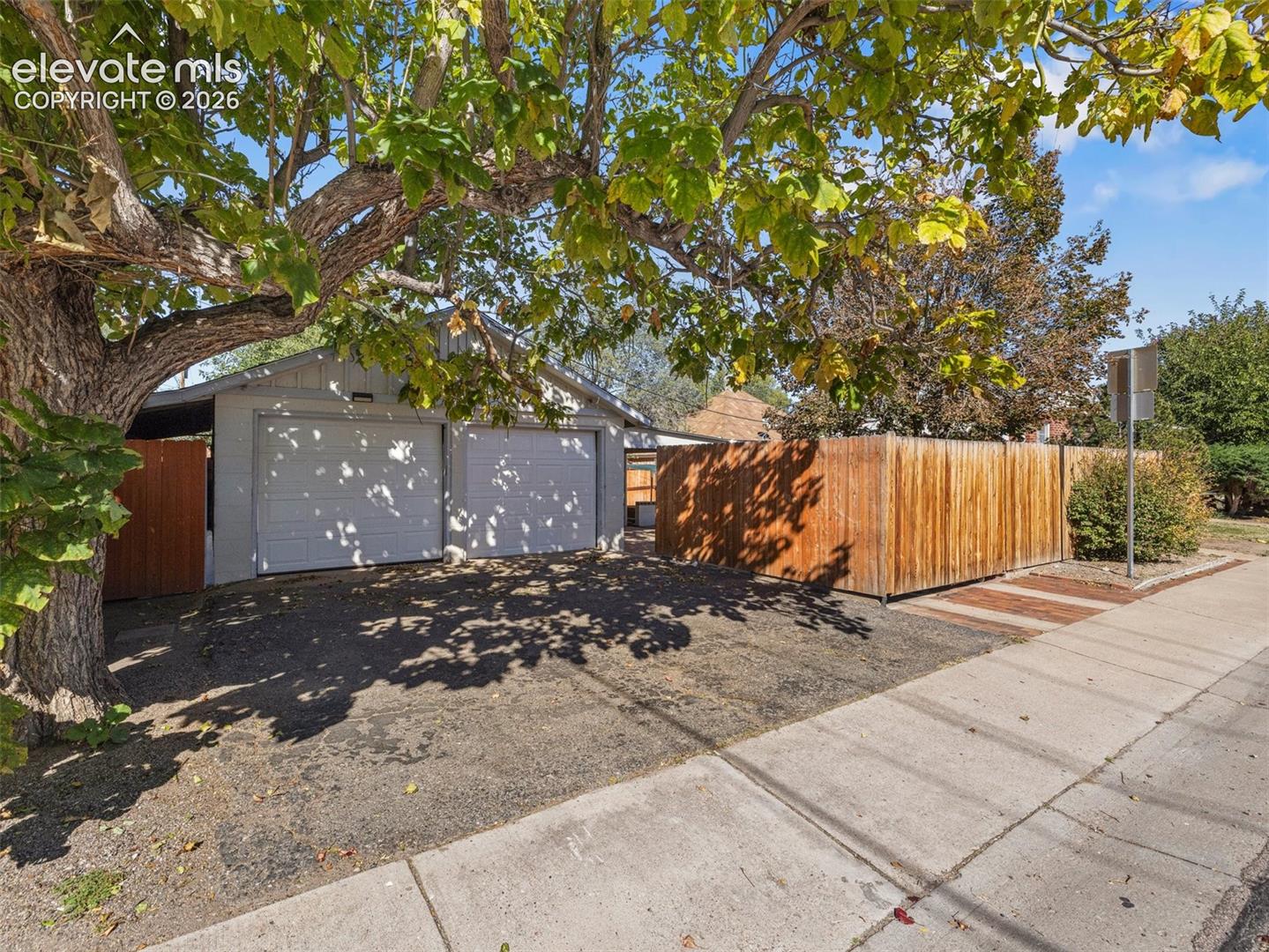 Detached two-car garage featuring dual white metal overhead doors, asphalt parking area, and wood-panel fencing
