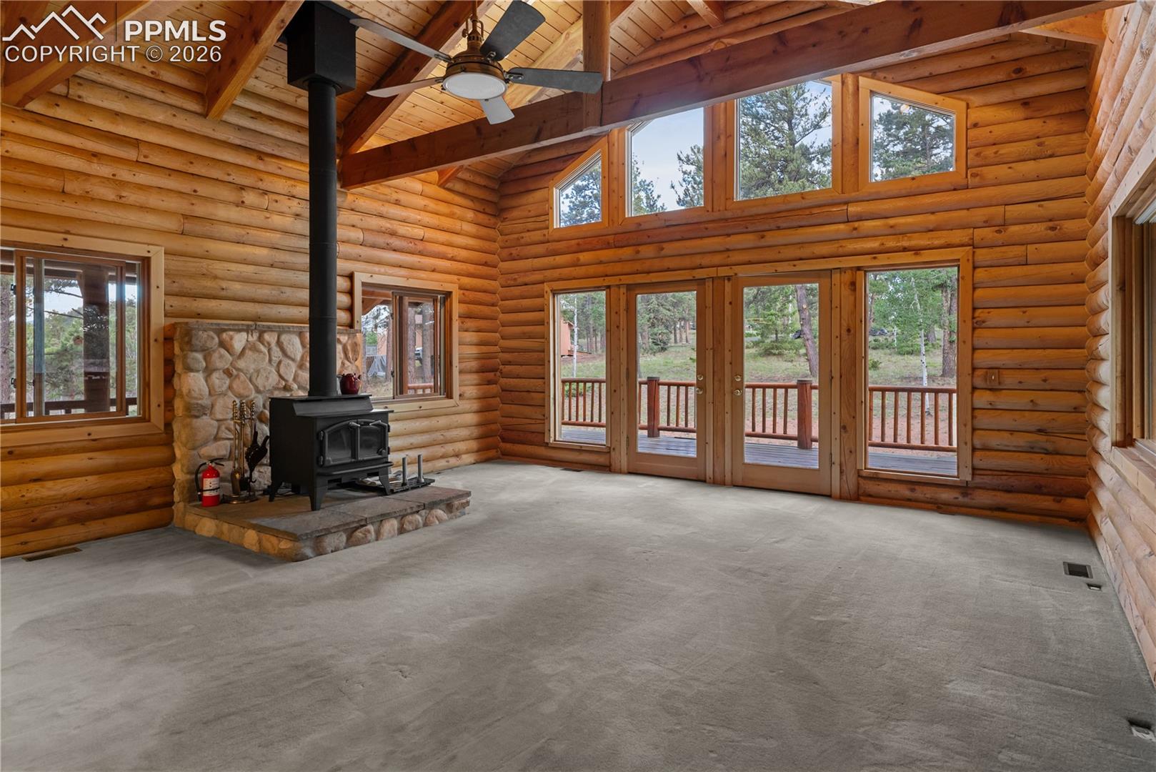 Unfurnished living room featuring a wood stove, a wood ceiling with exposed beams, high vaulted ceiling, ceiling fan, and carpet