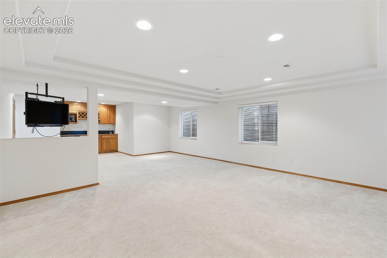 Expansive interior space featuring a recessed tray ceiling, integrated recessed lighting, wall-to-wall carpeting, and a built-in wet bar with wooden cabinetry