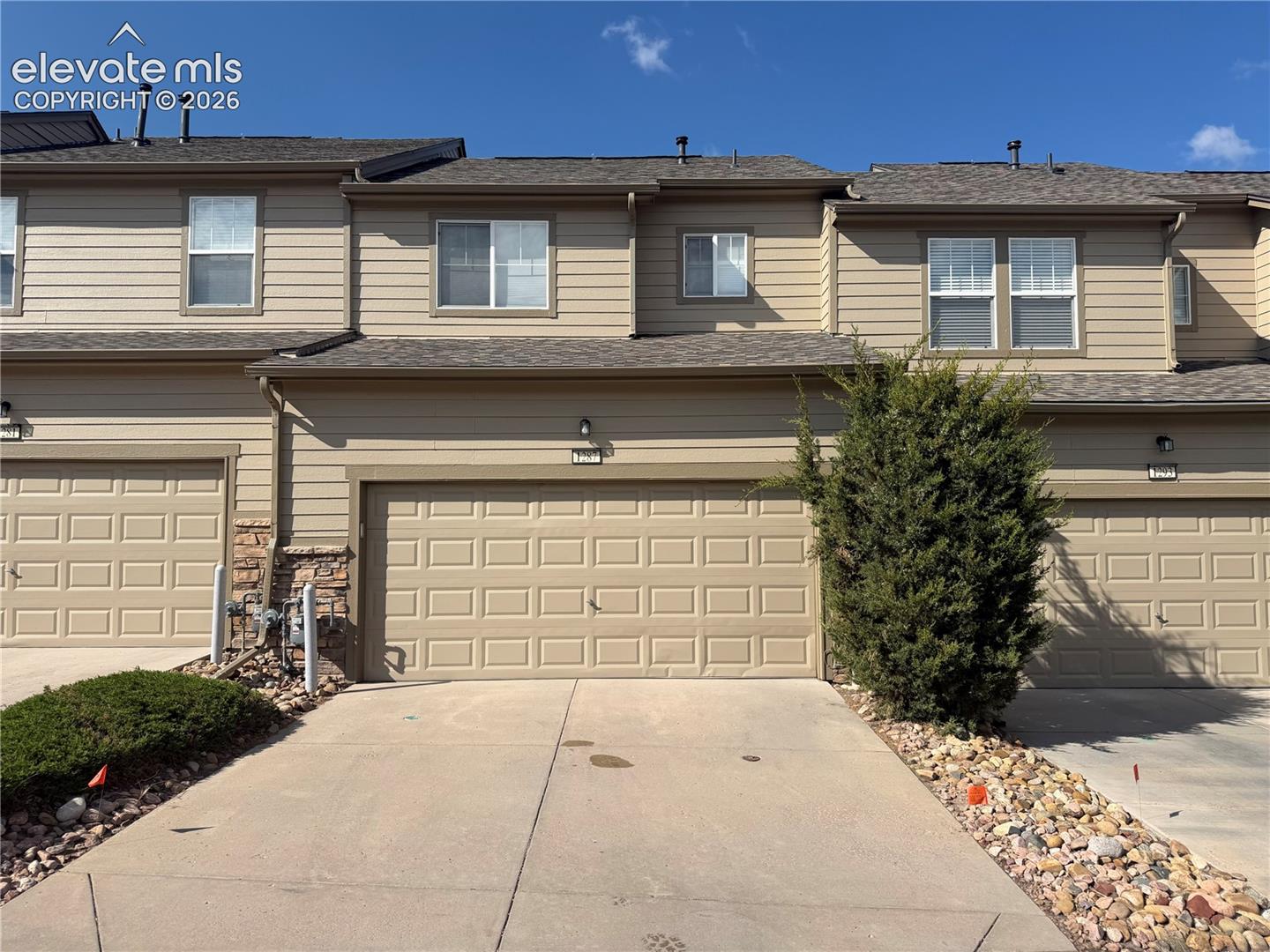 Beige horizontal siding exterior with a shingled roof, two attached garages, and a concrete driveway