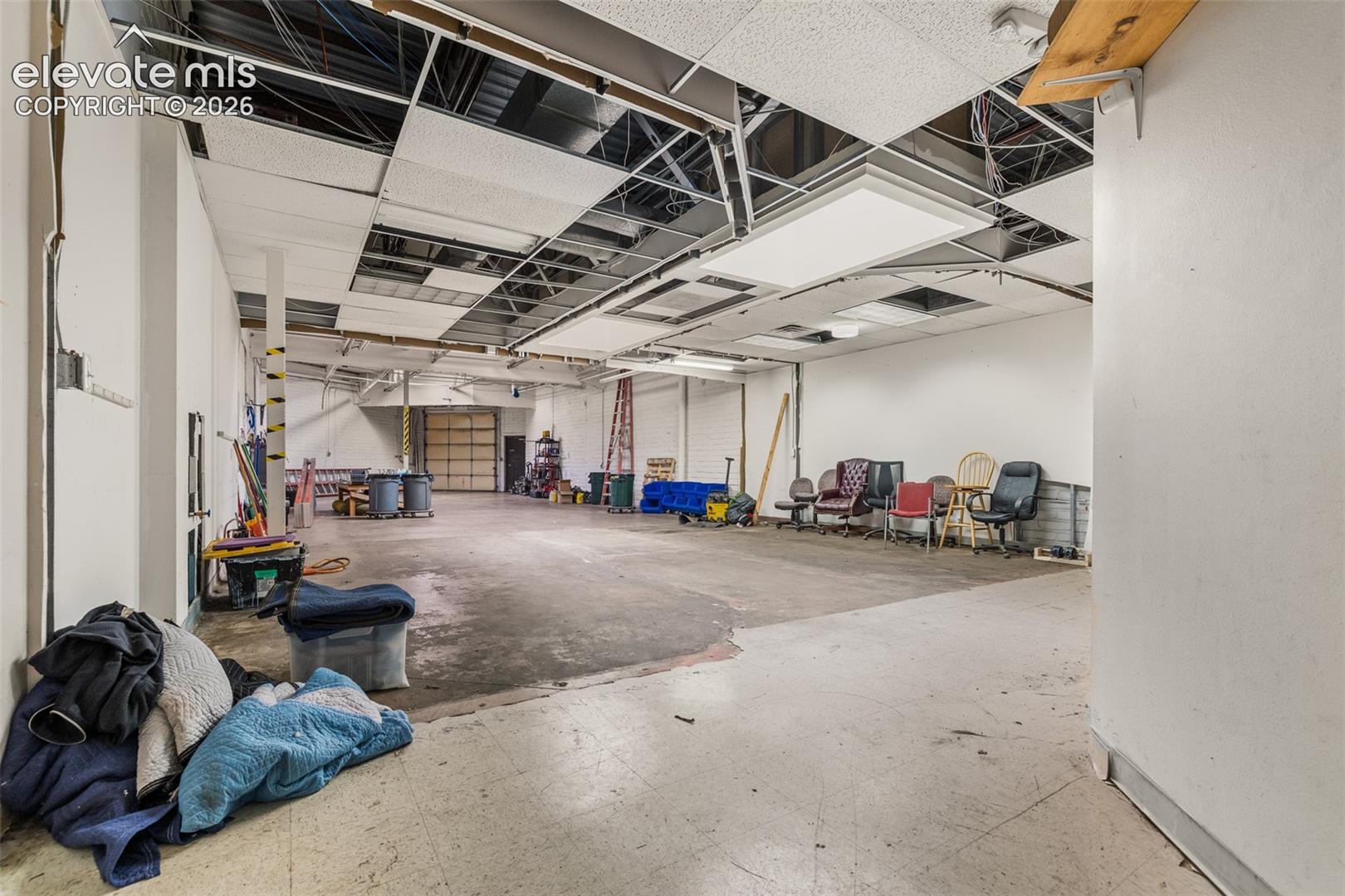 Open-concept industrial space featuring exposed ceiling joists, recessed panel lighting, concrete flooring, and a roll-up bay door
