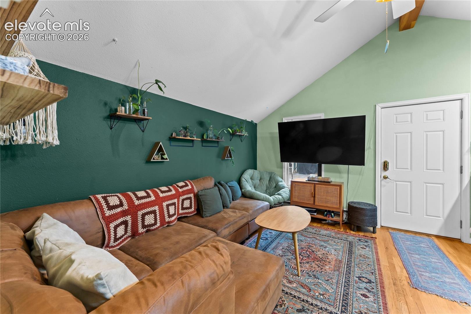 Vaulted ceiling featuring exposed wood beam, wood-finish flooring, and wall-mounted floating wood shelving
