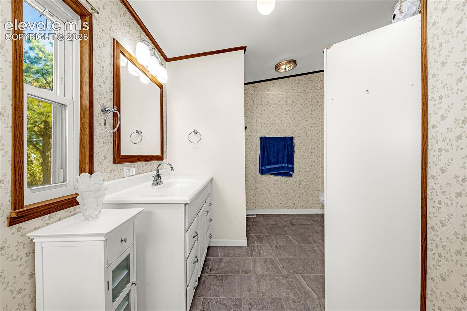 Bathroom featuring a white vanity cabinet, rectangular sink with chrome faucet, wall-mounted mirror, and tile-finish flooring