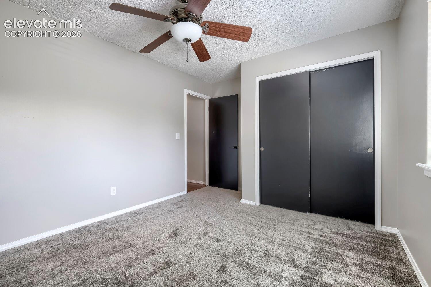 Neutral gray walls with white trim, gray carpet flooring, and a ceiling fan with wood-finish blades