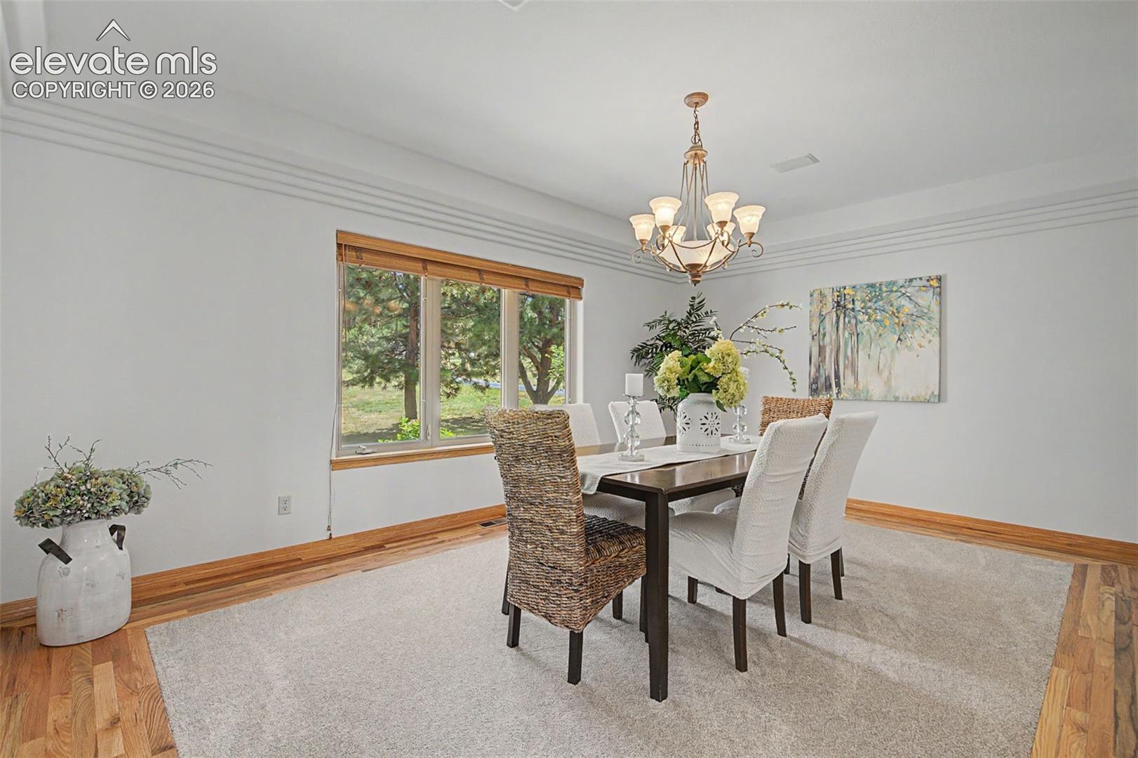 Dining space featuring wood-finish flooring, a multi-pane window with wood-tone blinds, an overhead chandelier, and extensive crown molding