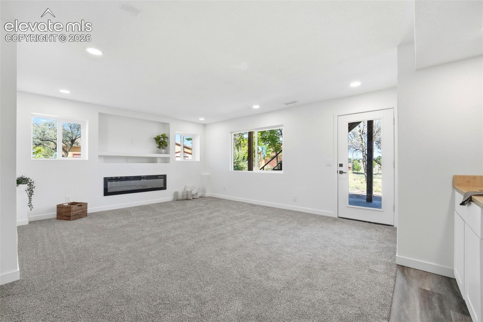 Spacious living area featuring light gray carpeting, a built-in electric fireplace, recessed lighting, and multiple windows