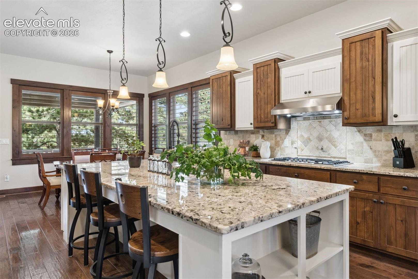 Kitchen featuring stone-finish countertops, two-tone wood and white cabinetry, a large central island with open shelving, diamond-pattern tile backsplash, and wood-finish flooring