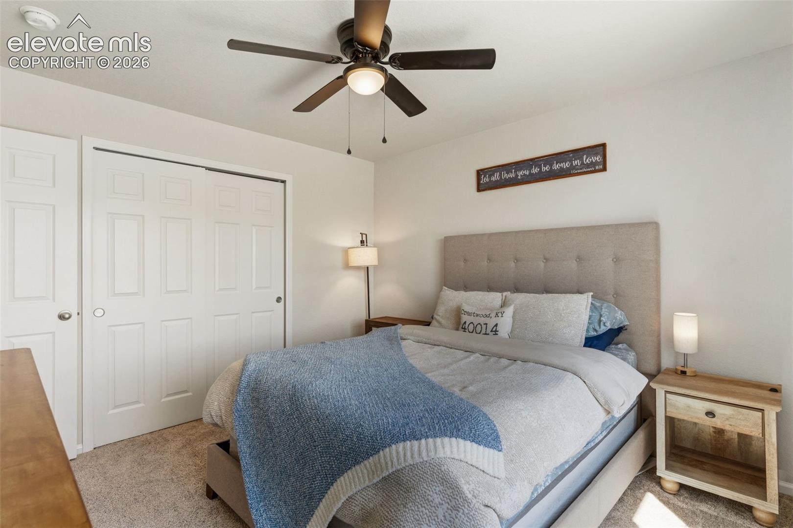 Carpeted bedroom featuring white walls, a multi-panel bifold closet door, and an overhead ceiling fan with lighting