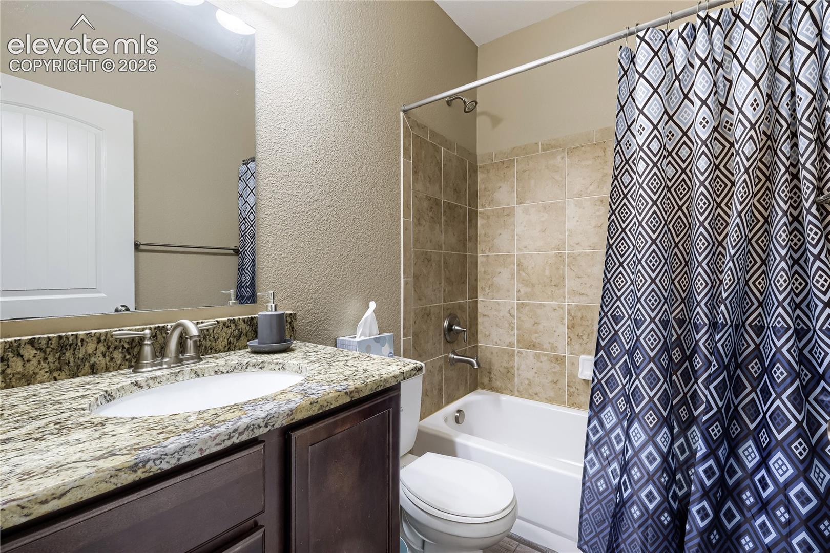 Basement full bathroom featuring a dark wood-finish vanity with a granite countertop, undermount sink, and brushed nickel faucet