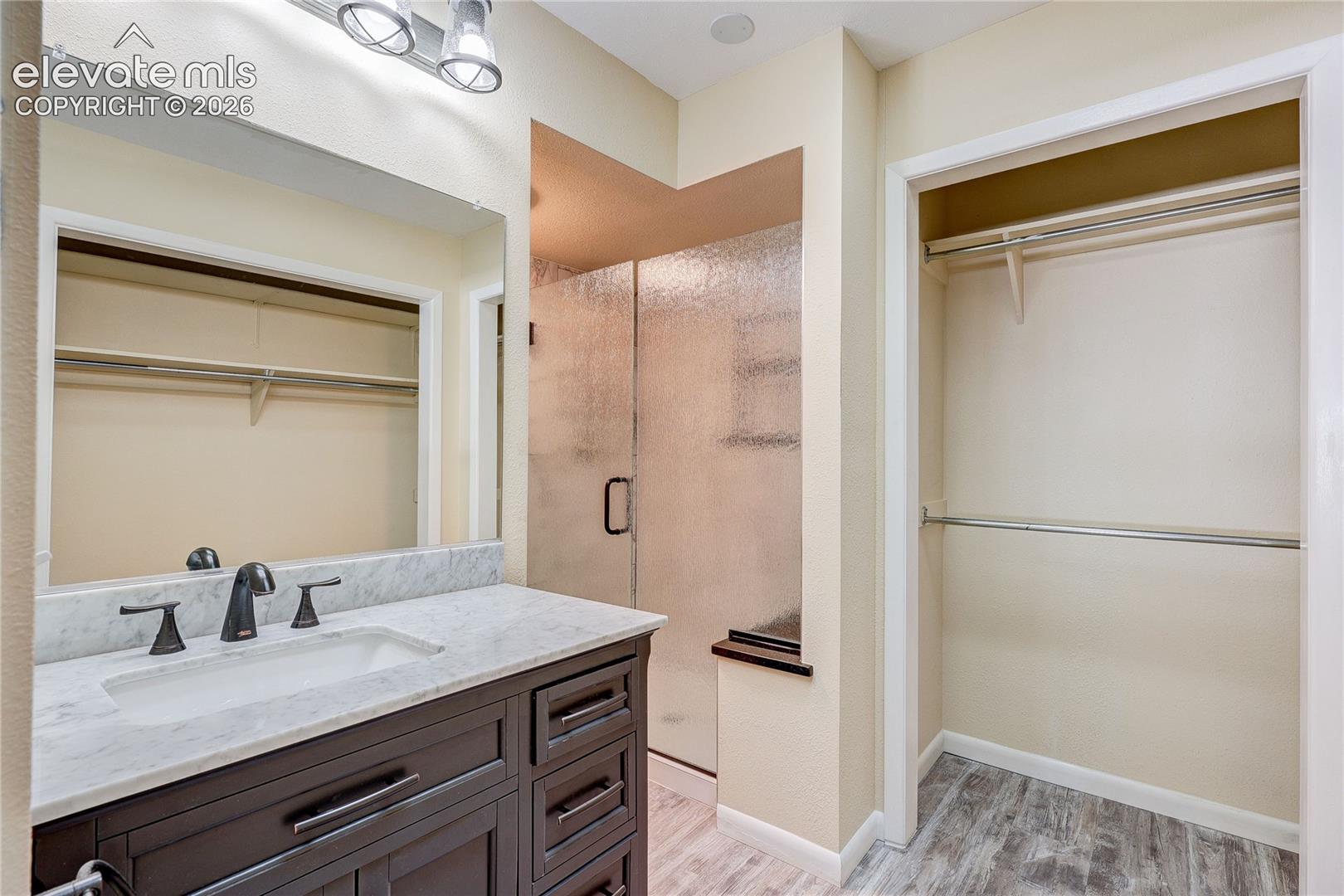 Dark-finished vanity cabinetry with a stone countertop, undermount sink, matte black faucet, glass-enclosed shower, and built-in closet storage