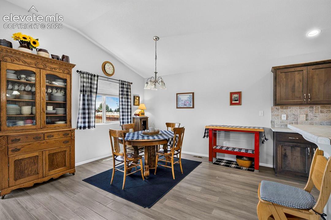 Dining area featuring vaulted ceilings, wood-finish flooring, and a large window