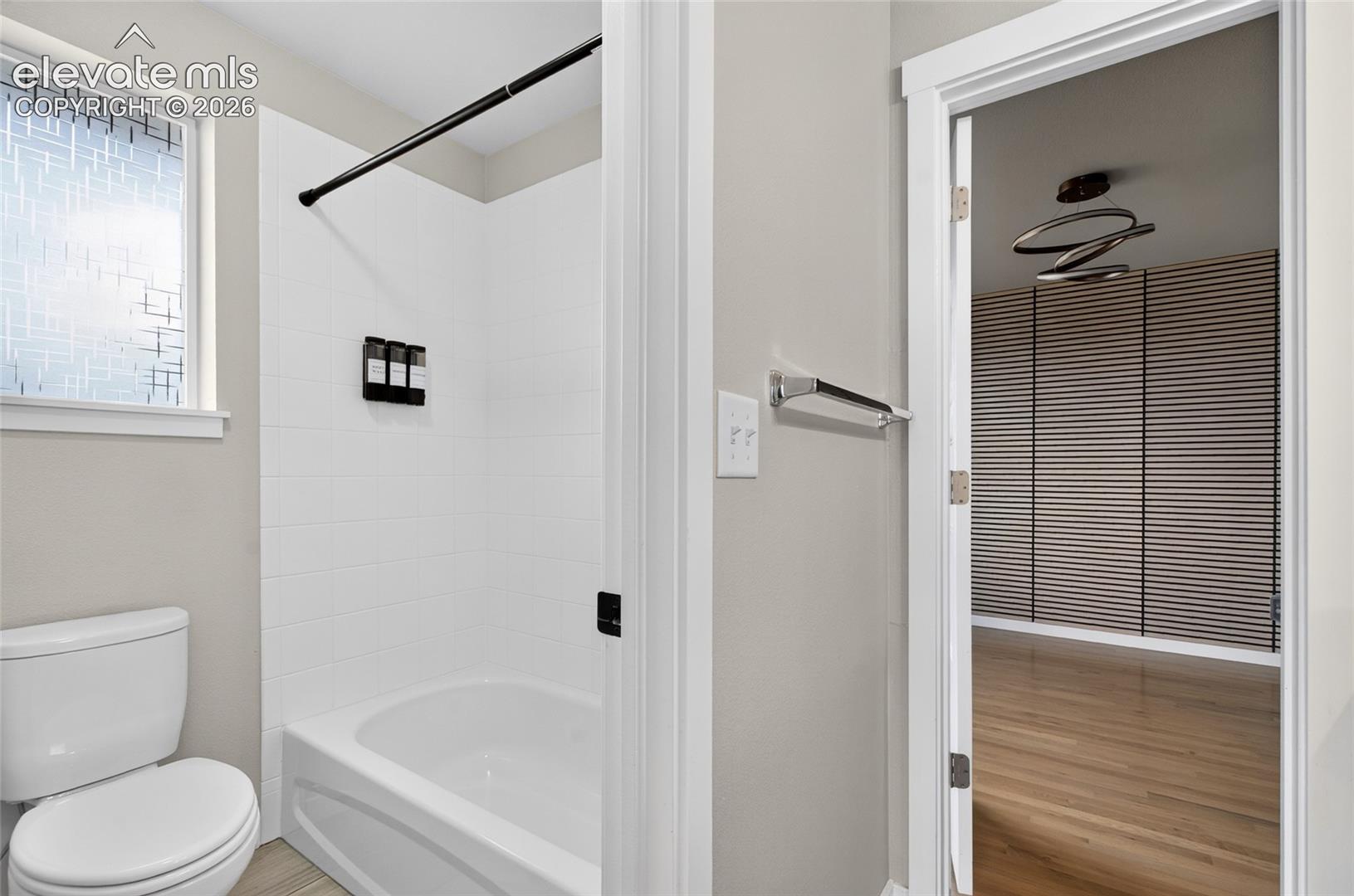 Bathroom featuring a white bathtub with subway tile surround, black shower hardware, and a toilet