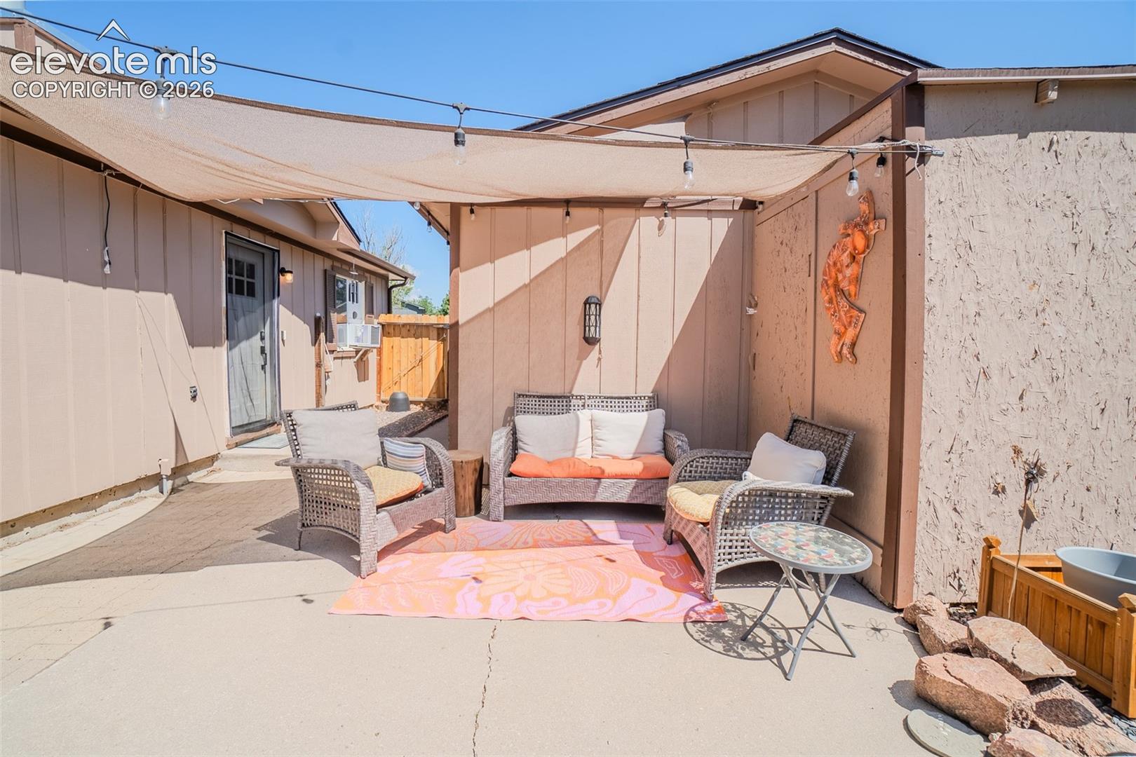 Paved patio area featuring a shade sail with string lighting, exterior wall lighting, and wood-paneled siding