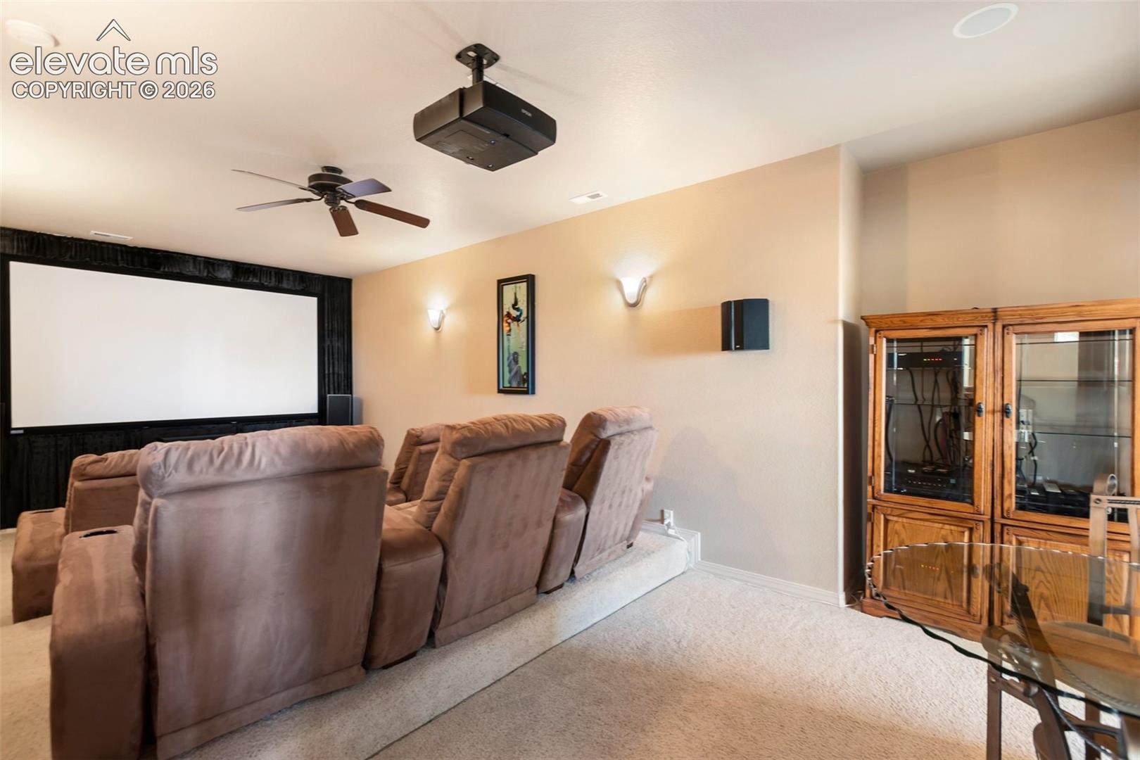 Media room featuring a ceiling-mounted projector, wall-mounted screen, built-in recessed lighting, integrated wall sconces, and a raised platform