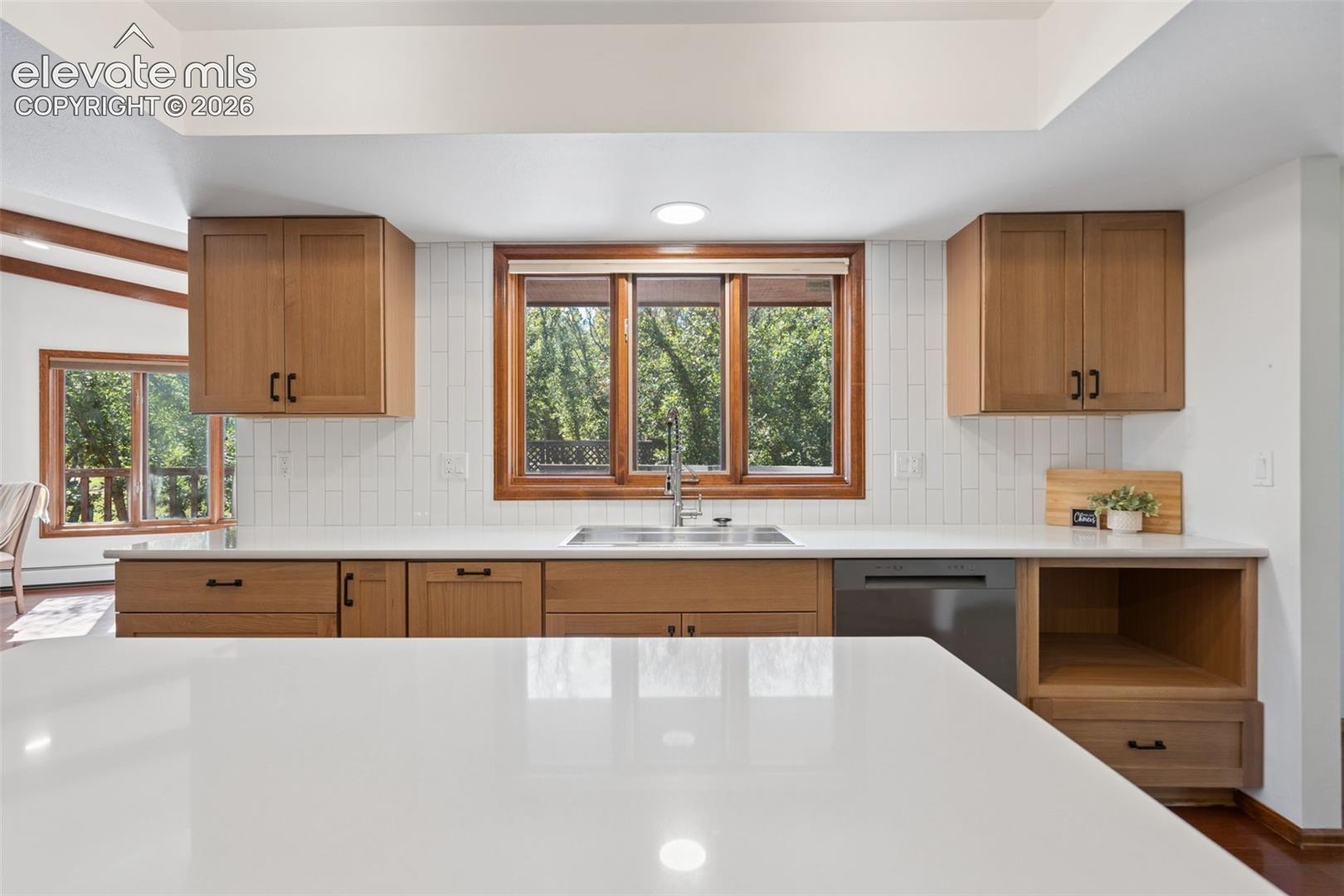 Kitchen featuring solid surface countertops, wood cabinetry, a stainless steel sink, and a tile backsplash