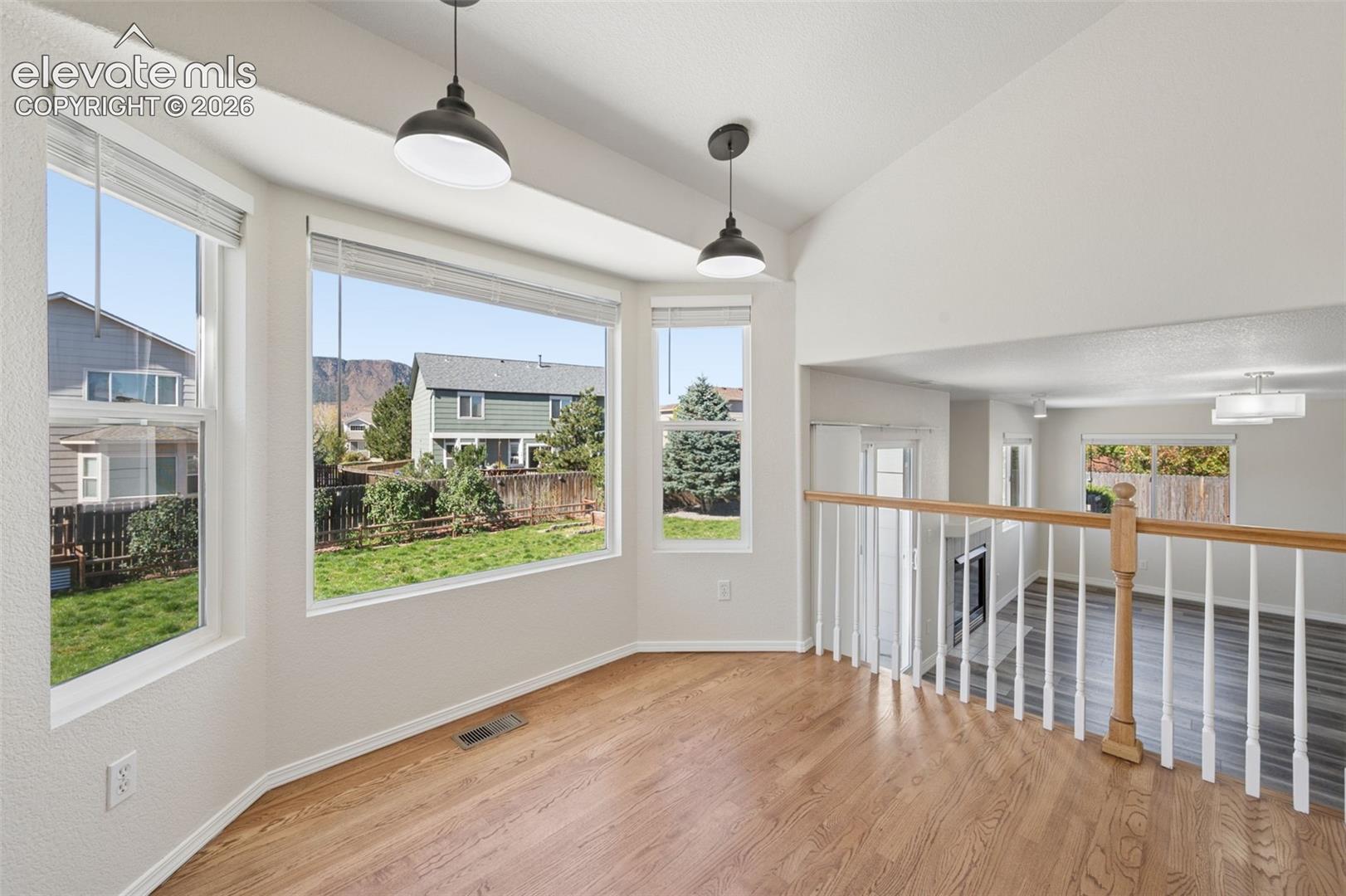 Bay window featuring natural light, wood-finish flooring, dual pendant lighting, and a wood-topped balustrade overlooking a lower level