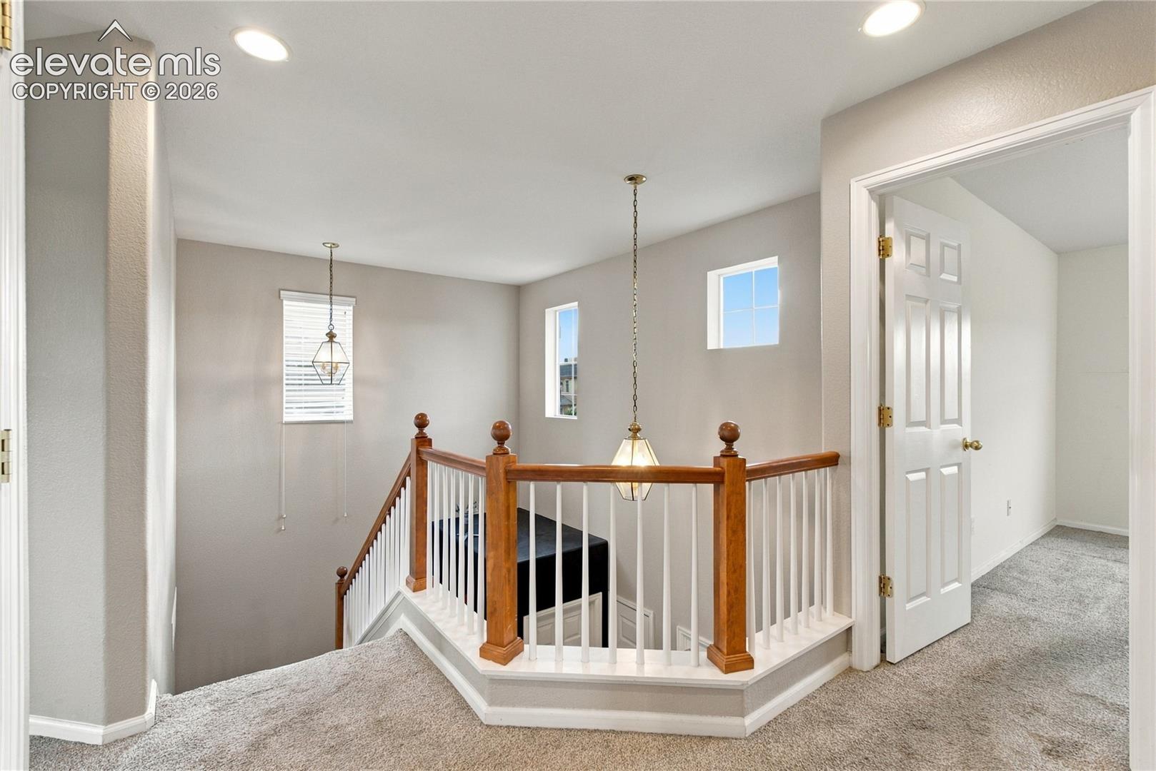 Landing area featuring wood-top railings with vertical balusters, two hanging pendant light fixtures, recessed ceiling lighting, and wall-to-wall carpeting