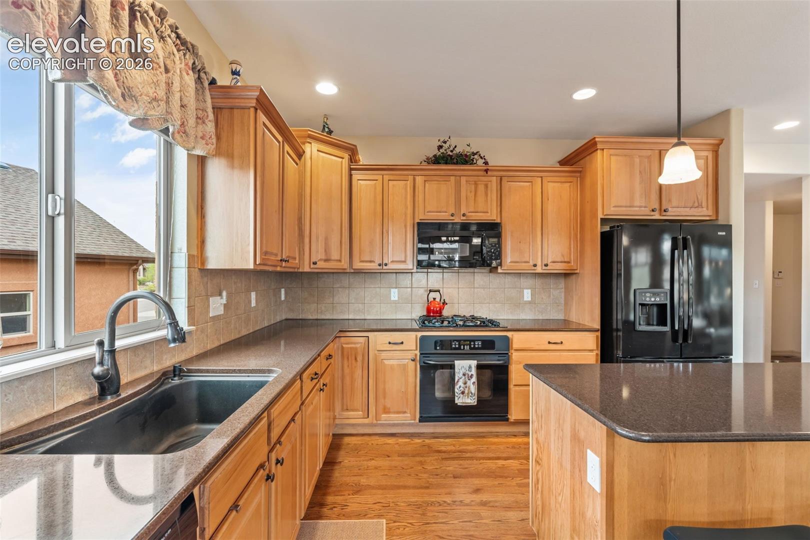 Kitchen featuring light wood cabinetry, dark countertops, a large window above the sink, a black gas range, and a black French door refrigerator