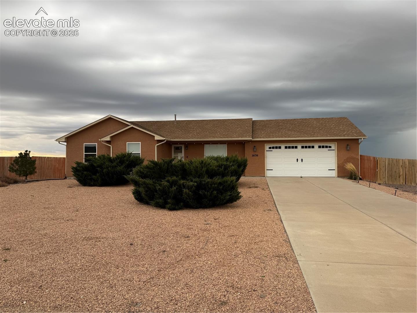 Single-story residence featuring a stucco exterior, asphalt shingle roof, two-car garage with white paneled door, concrete driveway, and xeriscape landscaping