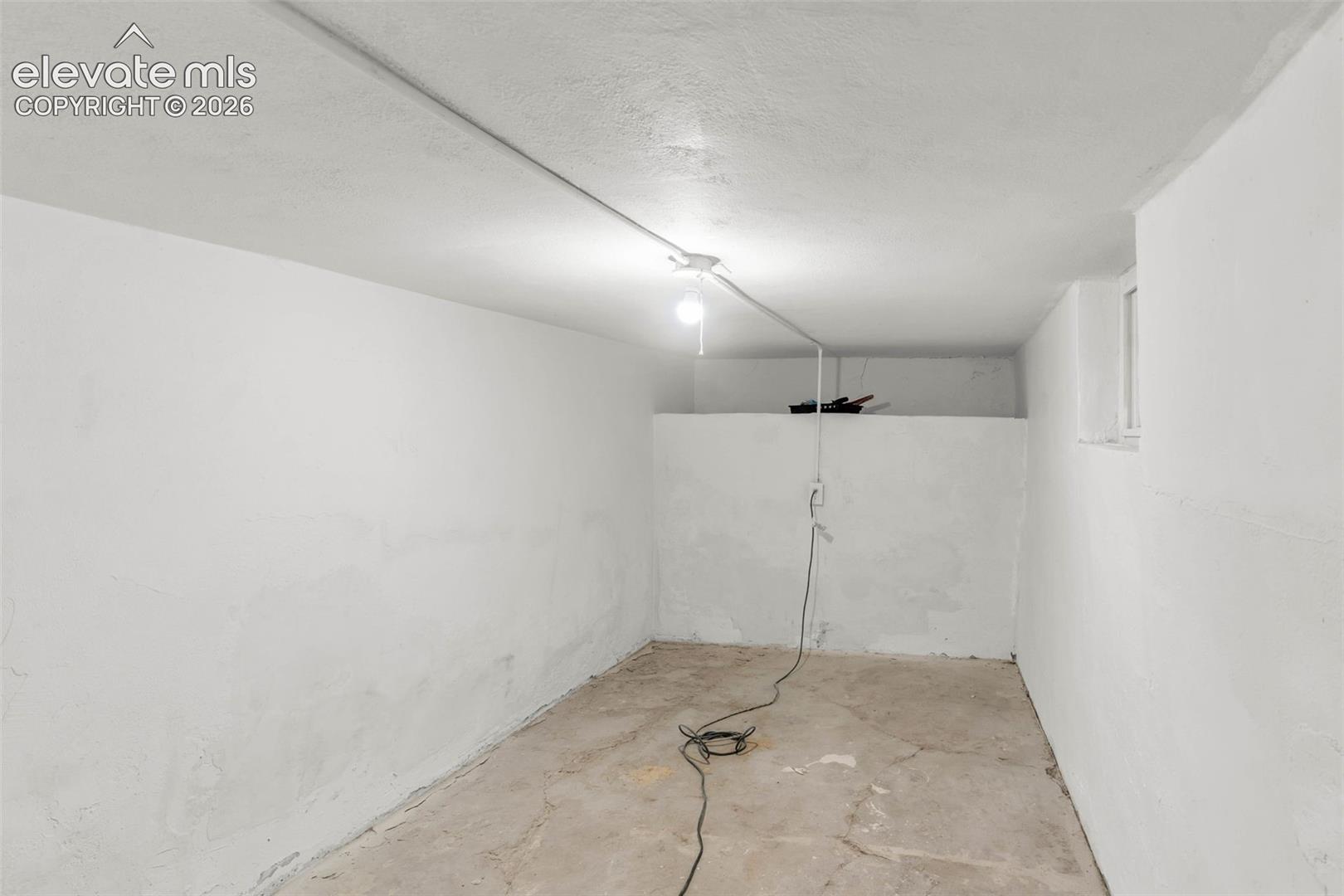 Storage area featuring painted concrete walls, exposed ceiling wiring, and a side-wall window