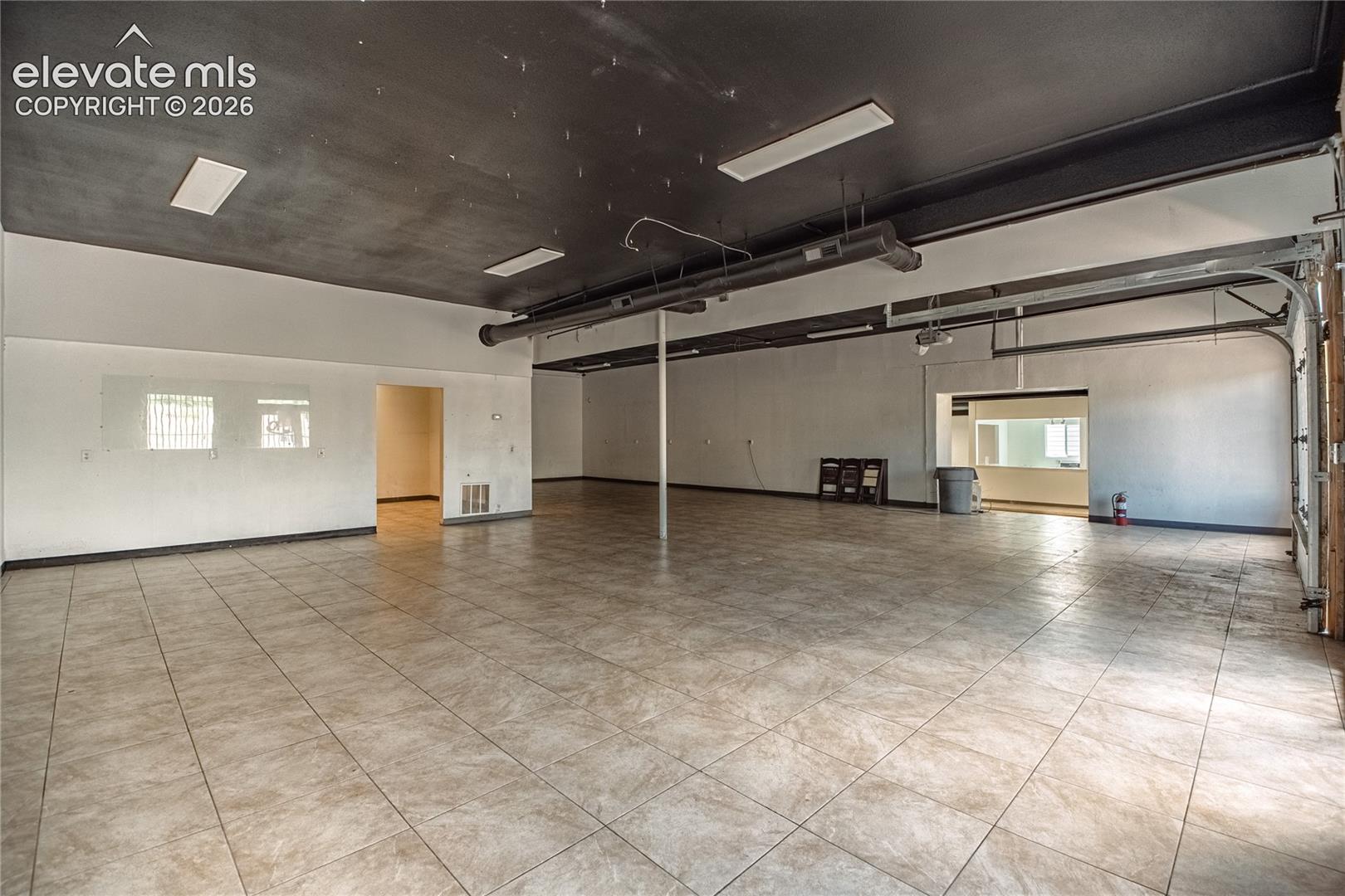 Spacious interior featuring tile flooring, exposed ductwork, recessed lighting, and a roll-up door