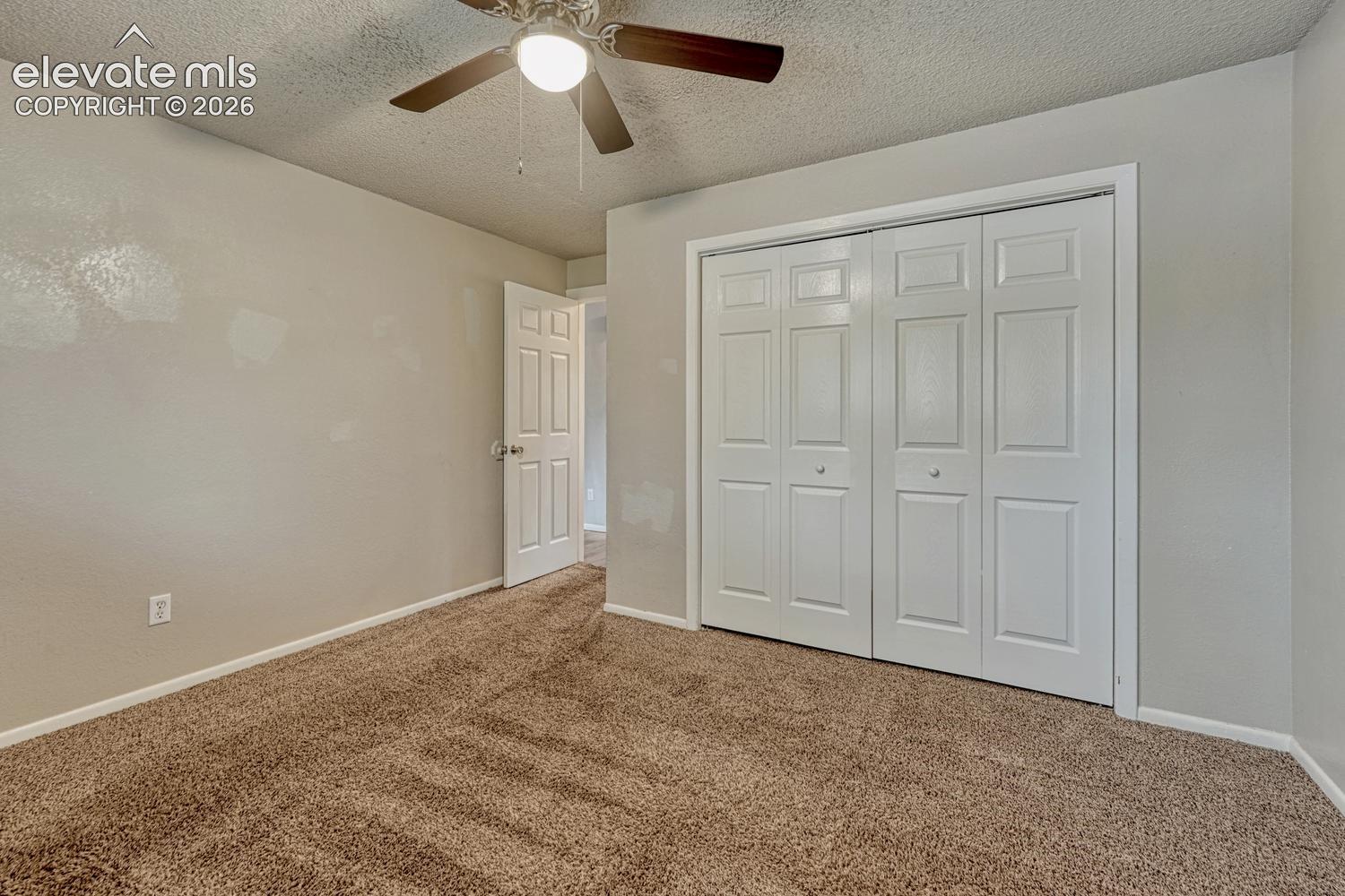 Textured wall finishes, brown carpet flooring, ceiling fan with integrated lighting, white paneled doors, and a bi-fold closet