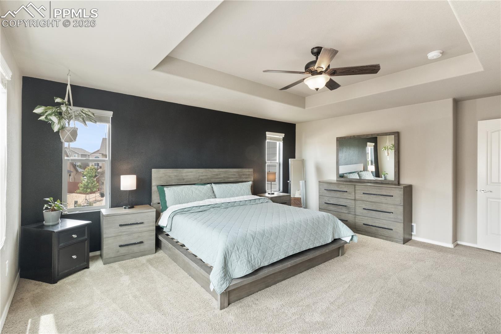 Bedroom featuring light carpet, a ceiling fan, and a raised ceiling