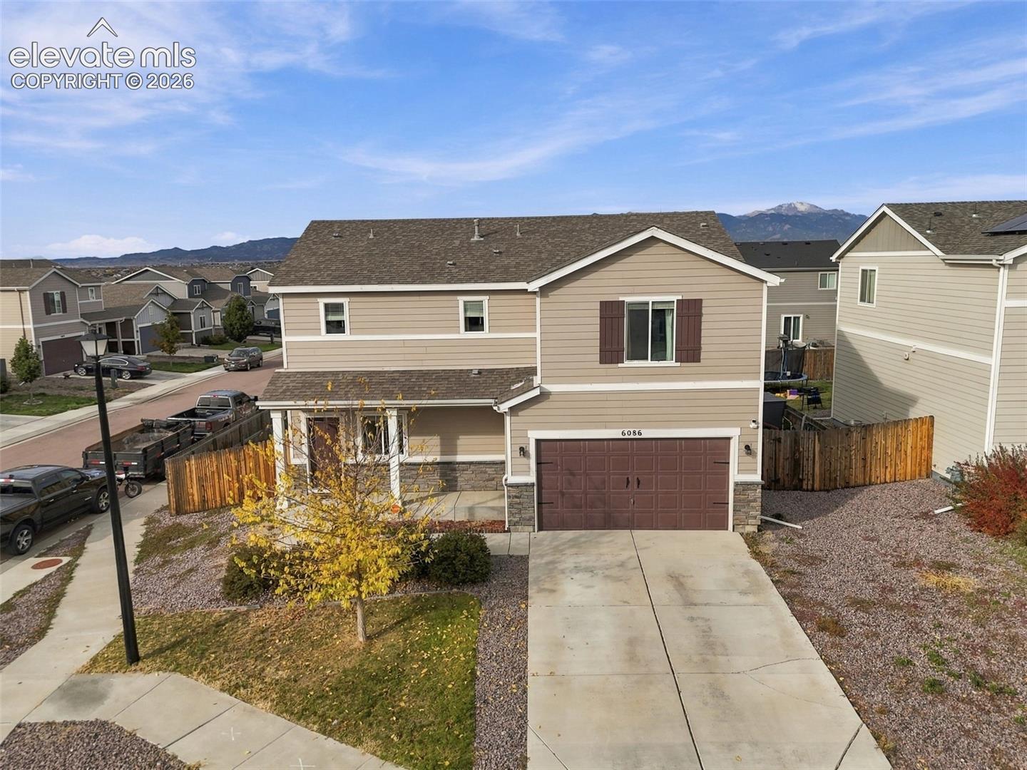 Two-story residence with horizontal siding, stone veneer accents, an attached two-car garage, and mountain backdrop