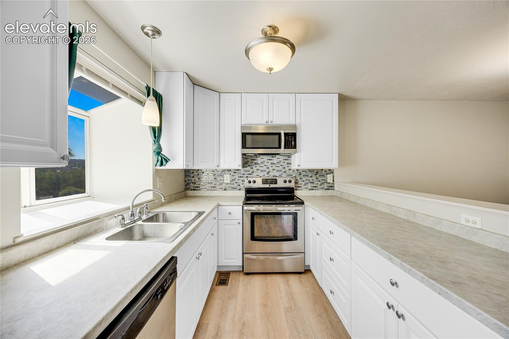White cabinetry, stainless steel appliances, mosaic tile backsplash, double basin sink, and wood-finish flooring