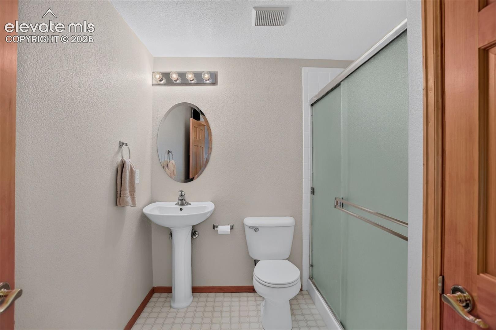 Full bathroom featuring a pedestal sink, oval mirror, and a shower with frosted glass sliding doors