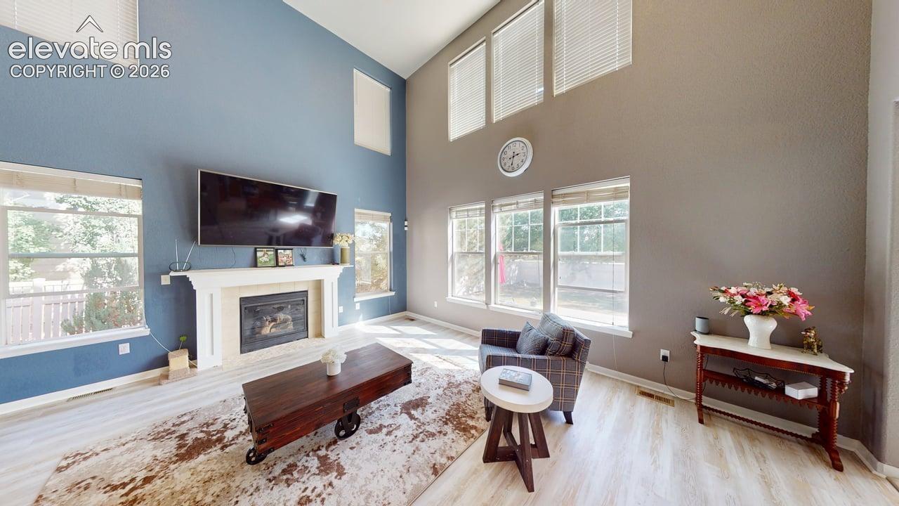 Two-story living area featuring a fireplace with a white mantel, high ceilings, large windows, and light wood-finish flooring