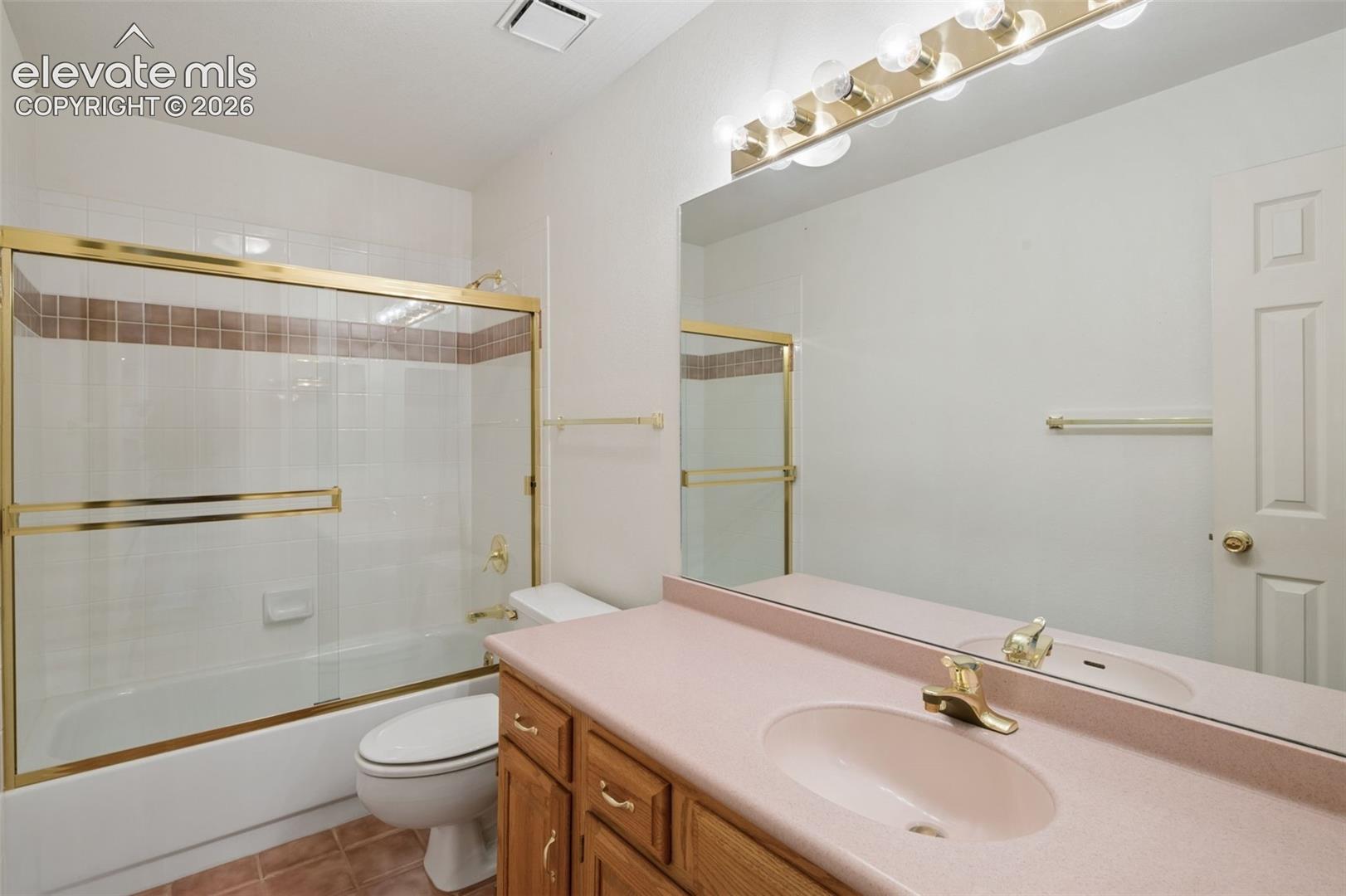 Bathroom featuring a vanity with a solid-surface countertop and integrated sink, wooden cabinetry, a large wall-mounted mirror, brass-finish hardware, and a tub-shower combination with a glass sliding enclosure