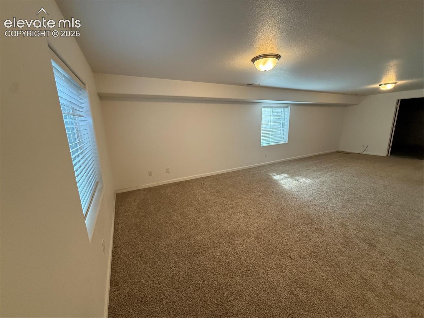 Open-concept interior featuring neutral wall-to-wall carpeting, dual flush-mount ceiling light fixtures, and multiple windows with white horizontal blinds