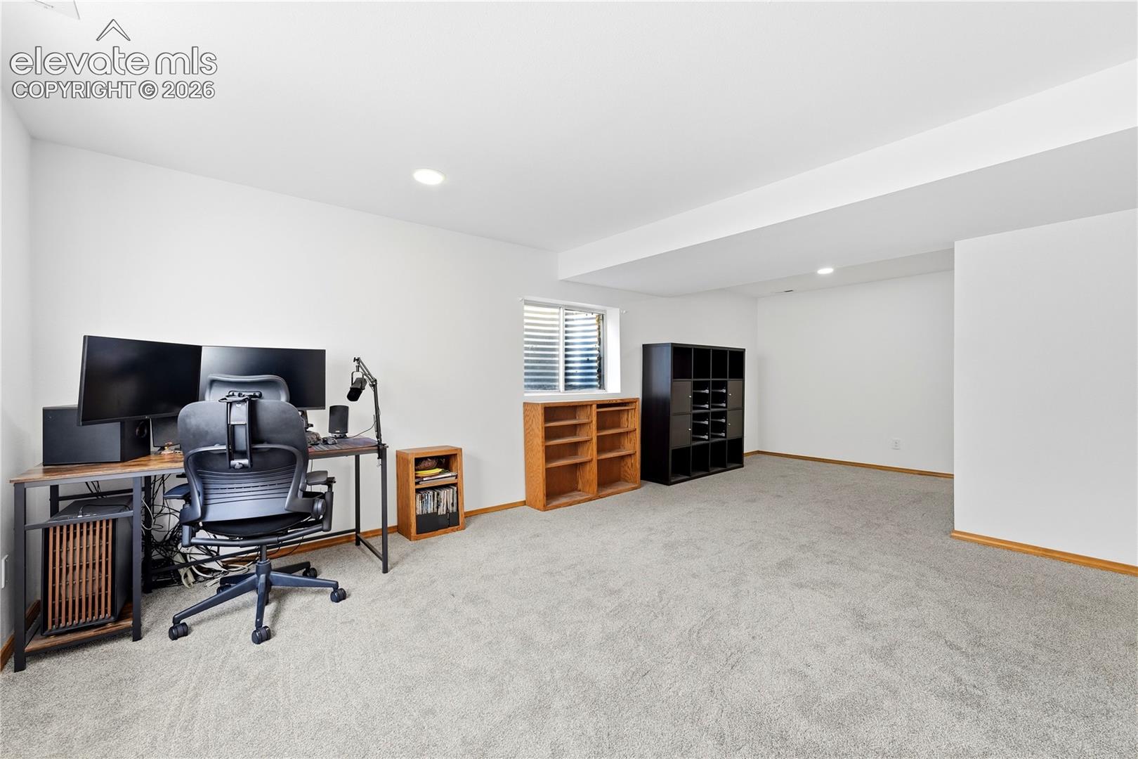 Spacious room featuring light-colored carpeting, white walls, recessed lighting, and window wells