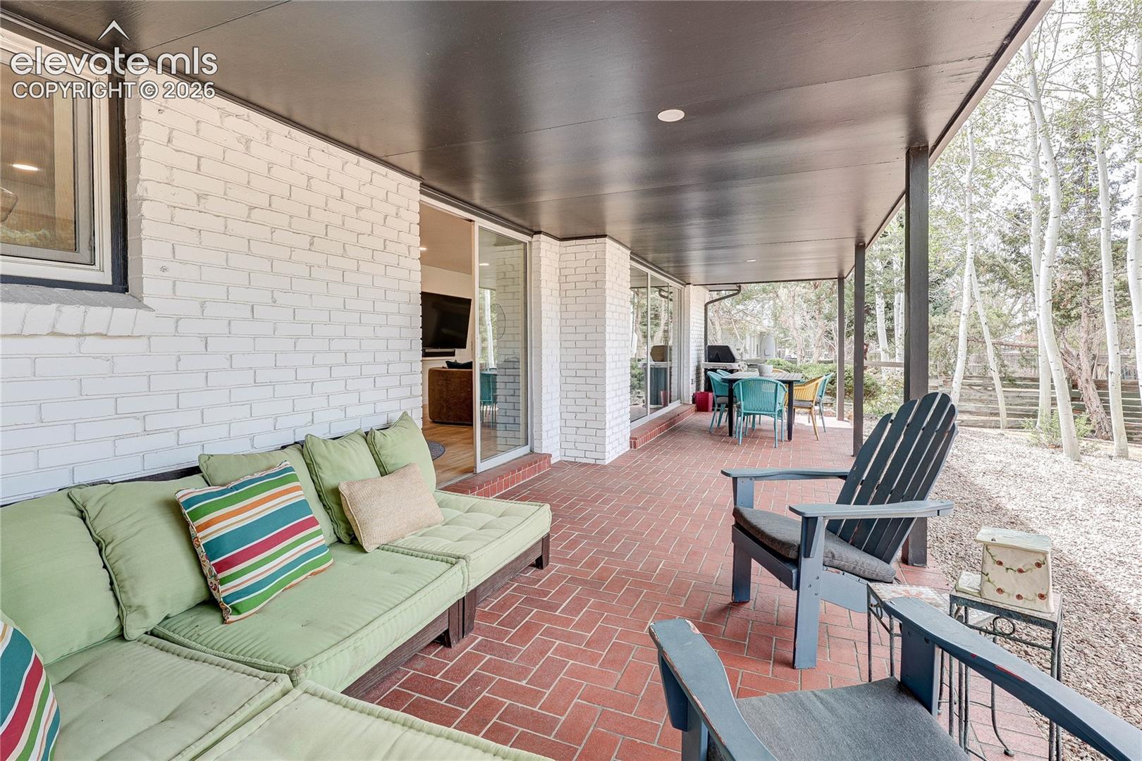 Covered patio featuring brick flooring and white painted brick exterior