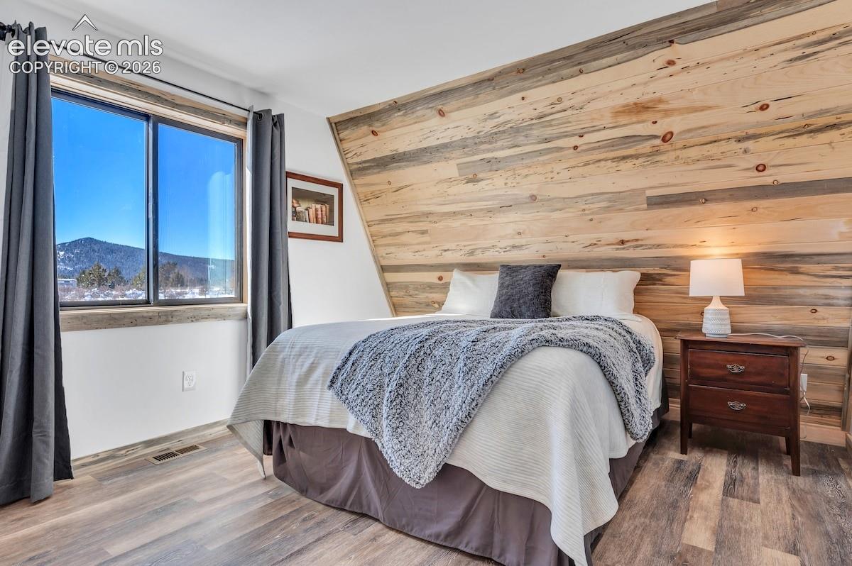 Sloped wall featuring natural wood-plank paneling, wood-finish flooring, and large window with mountain scenery